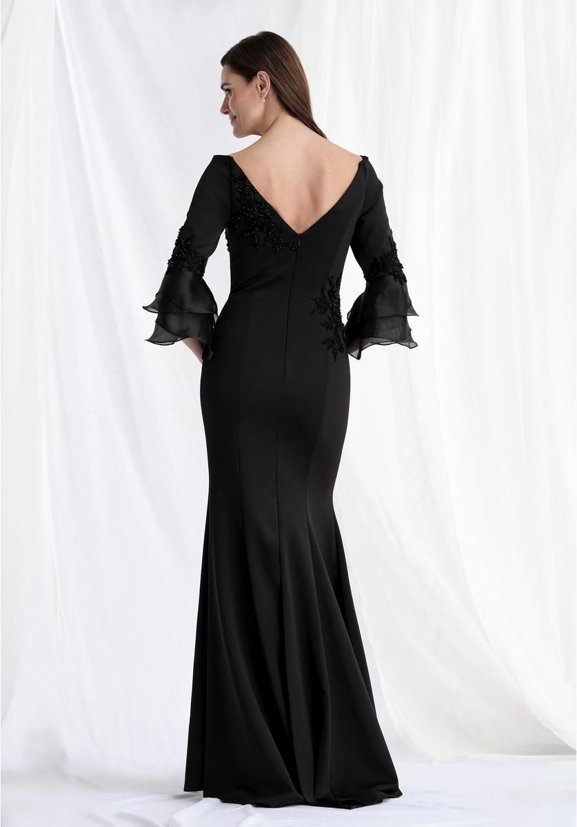 Woman in a black, floor-length gown with three-quarter sleeves, posed in front of a white backdrop.