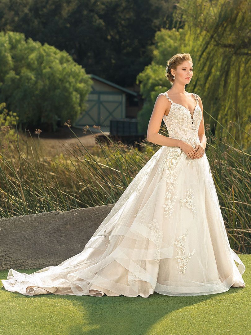 Woman in a wedding dress poses outside, a long train extending across the grass.