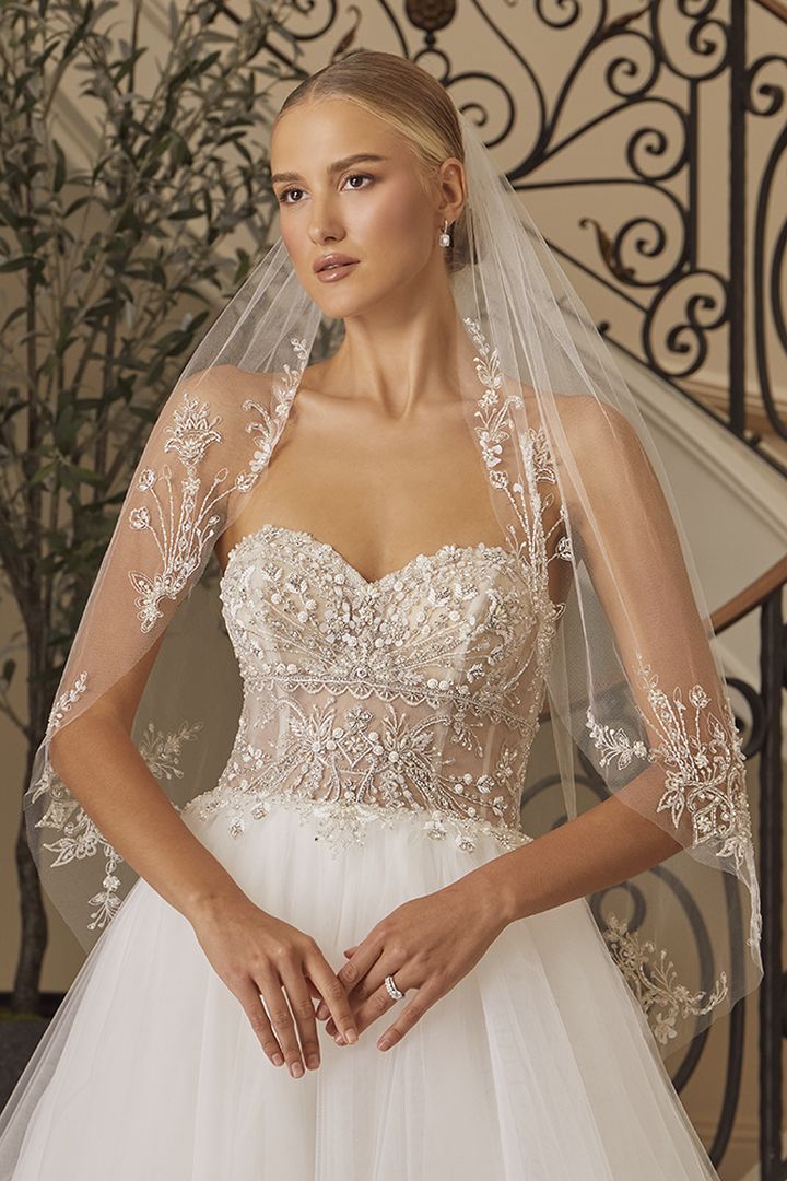 Woman in white beaded wedding dress with veil, indoors.