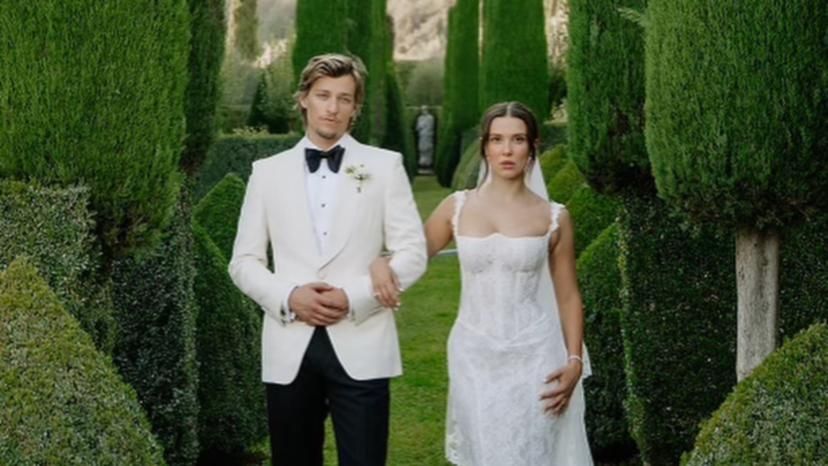 Couple in wedding attire walking through a garden, man in white suit, woman in white dress.