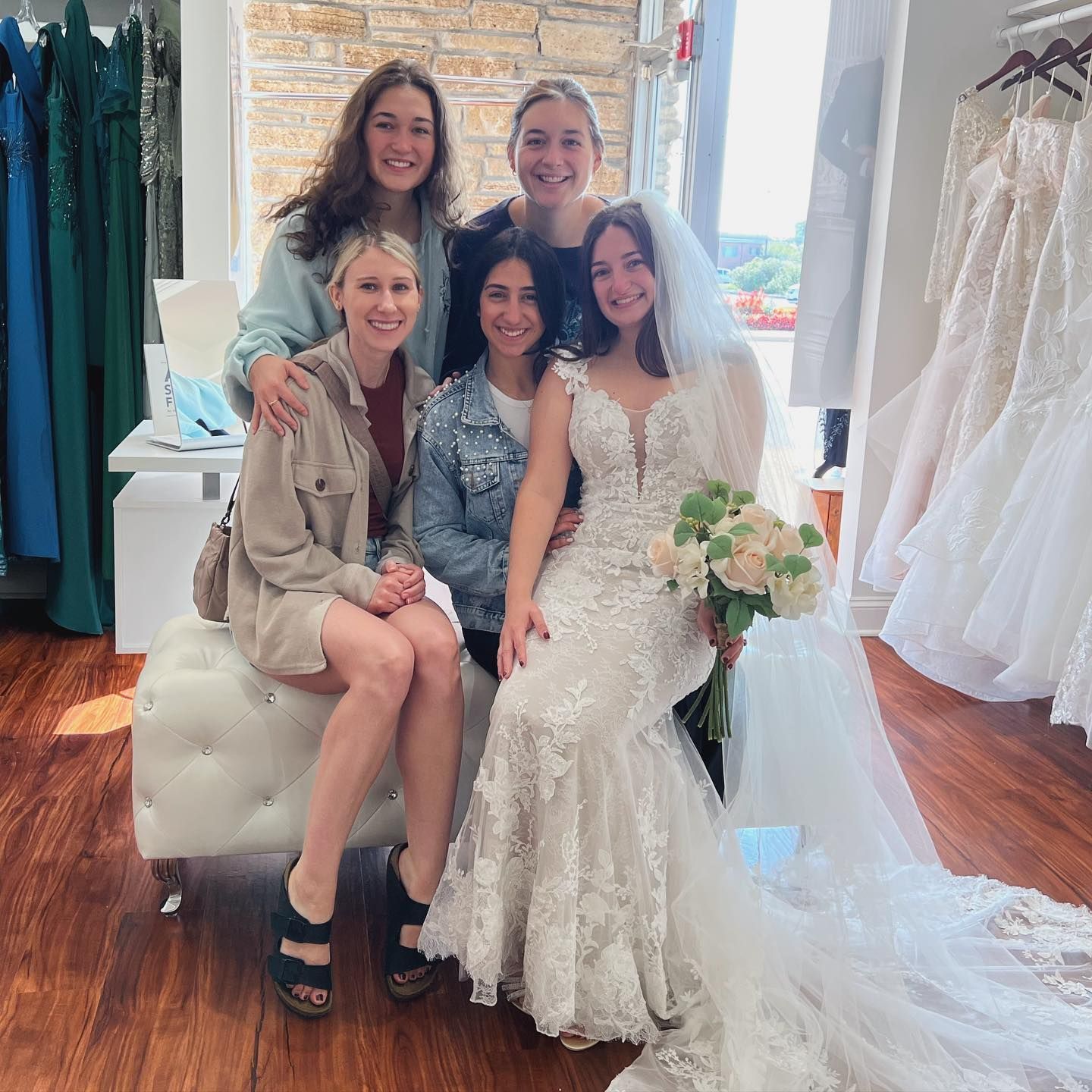 Bride in wedding dress with veil, surrounded by friends in a bridal shop.