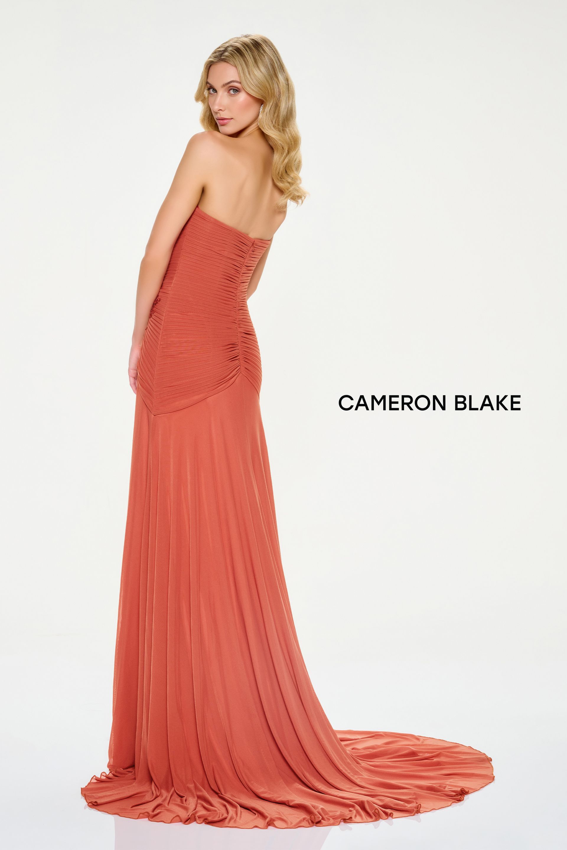 Woman wearing a strapless coral gown with pleated skirt, looking over her shoulder.