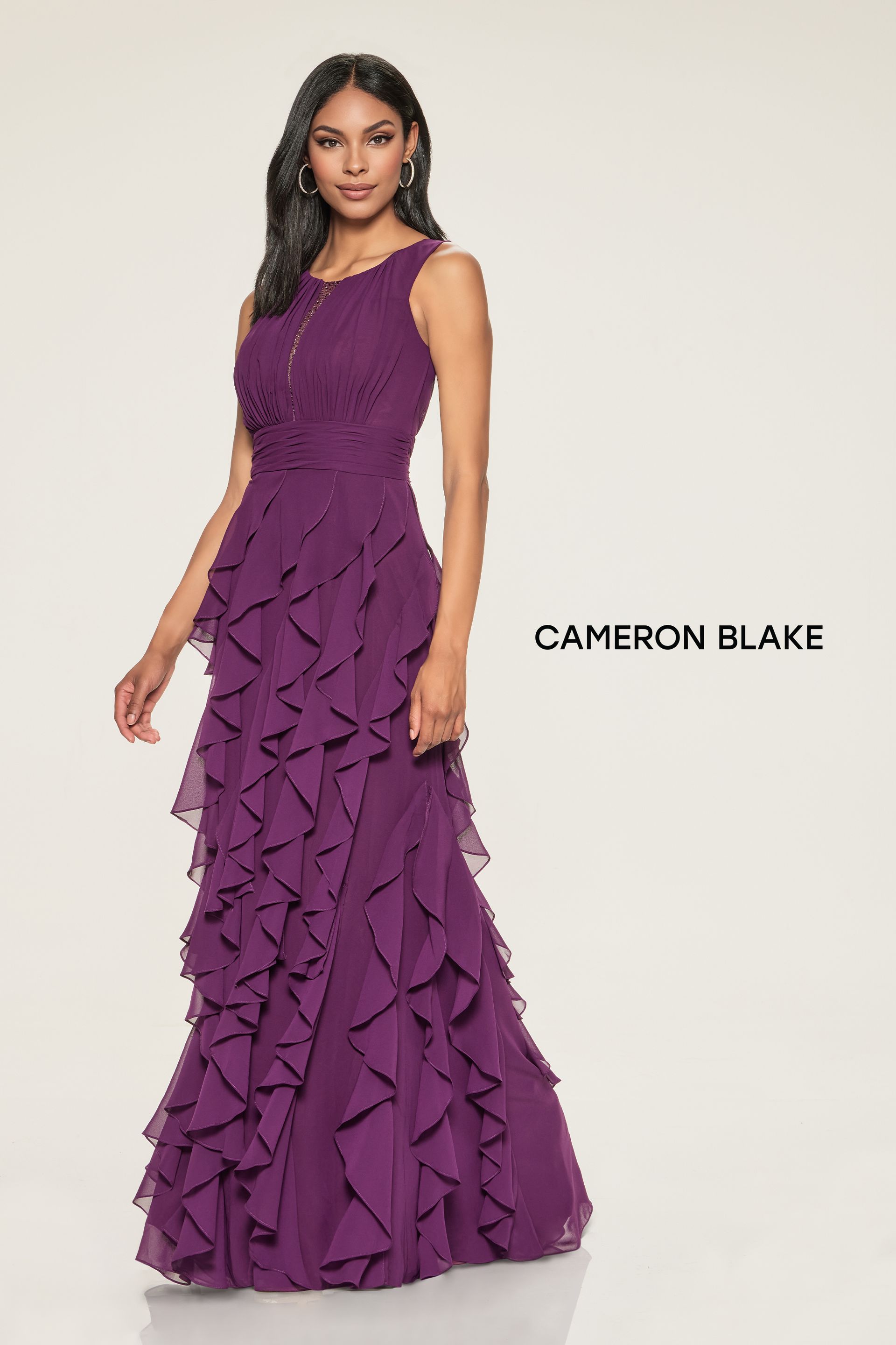 Woman in a dark purple formal gown with layered ruffles, standing in front of a white background.