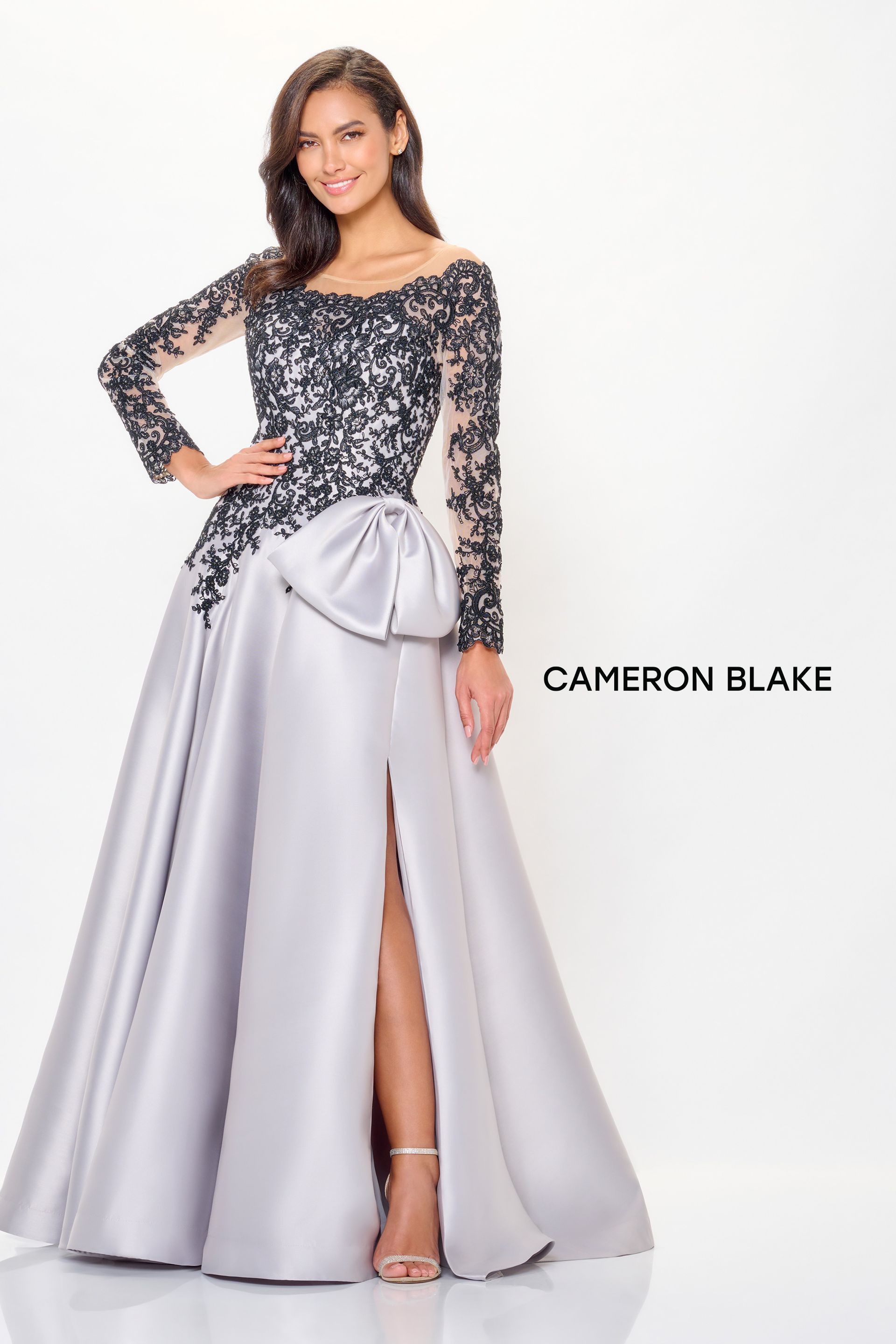 Woman in silver gown with black lace bodice, long sleeves, and thigh-high slit, posing.