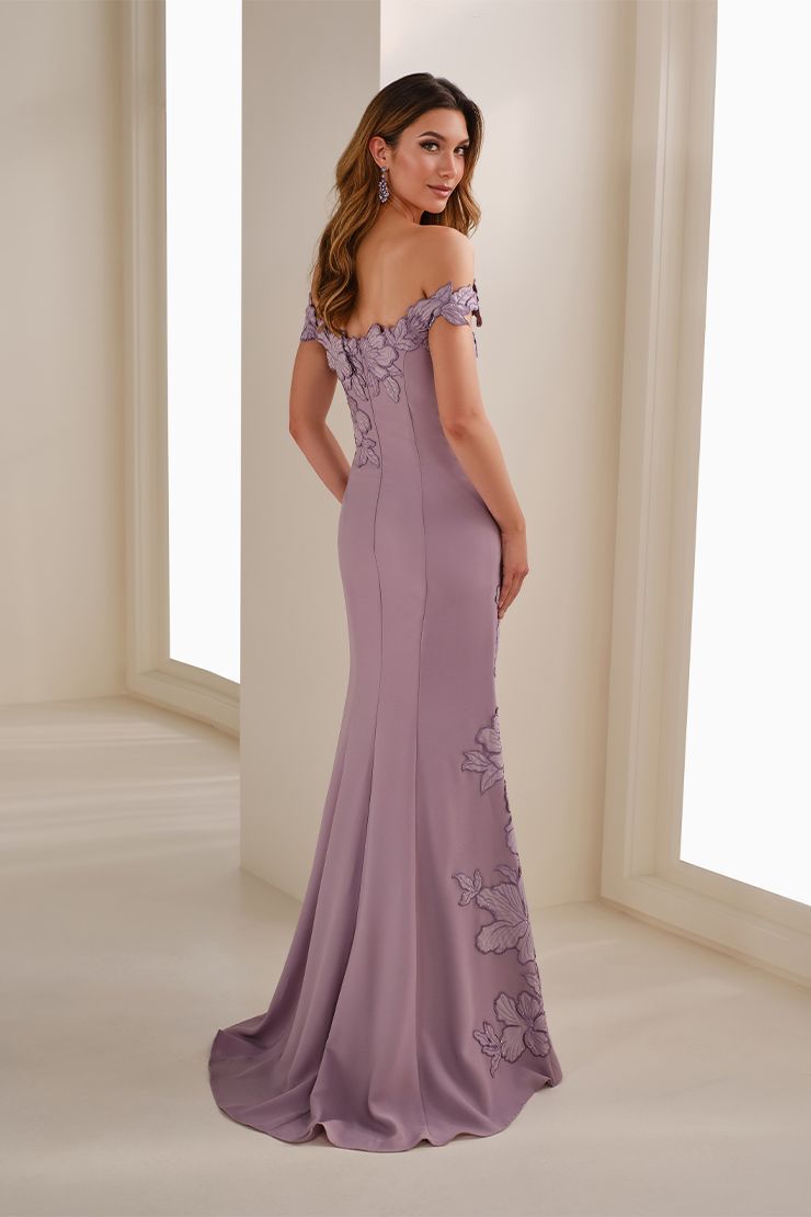 Woman in a pink off-shoulder lace gown standing by a window