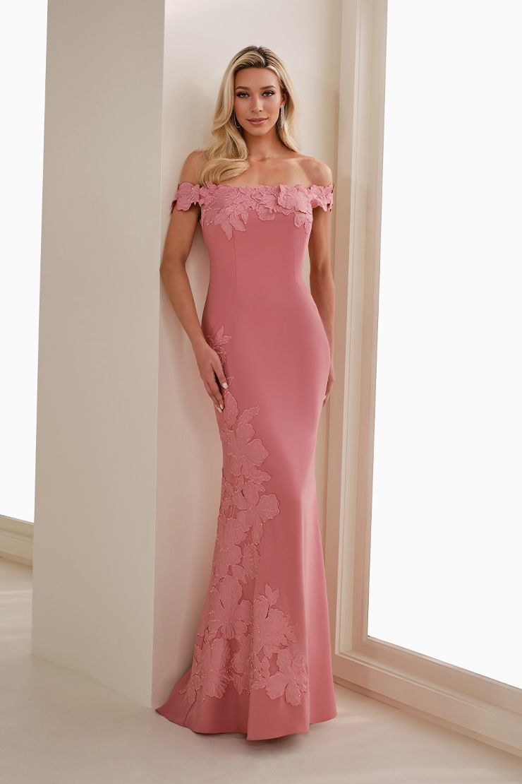 Woman in a pink off-shoulder lace gown standing by a window