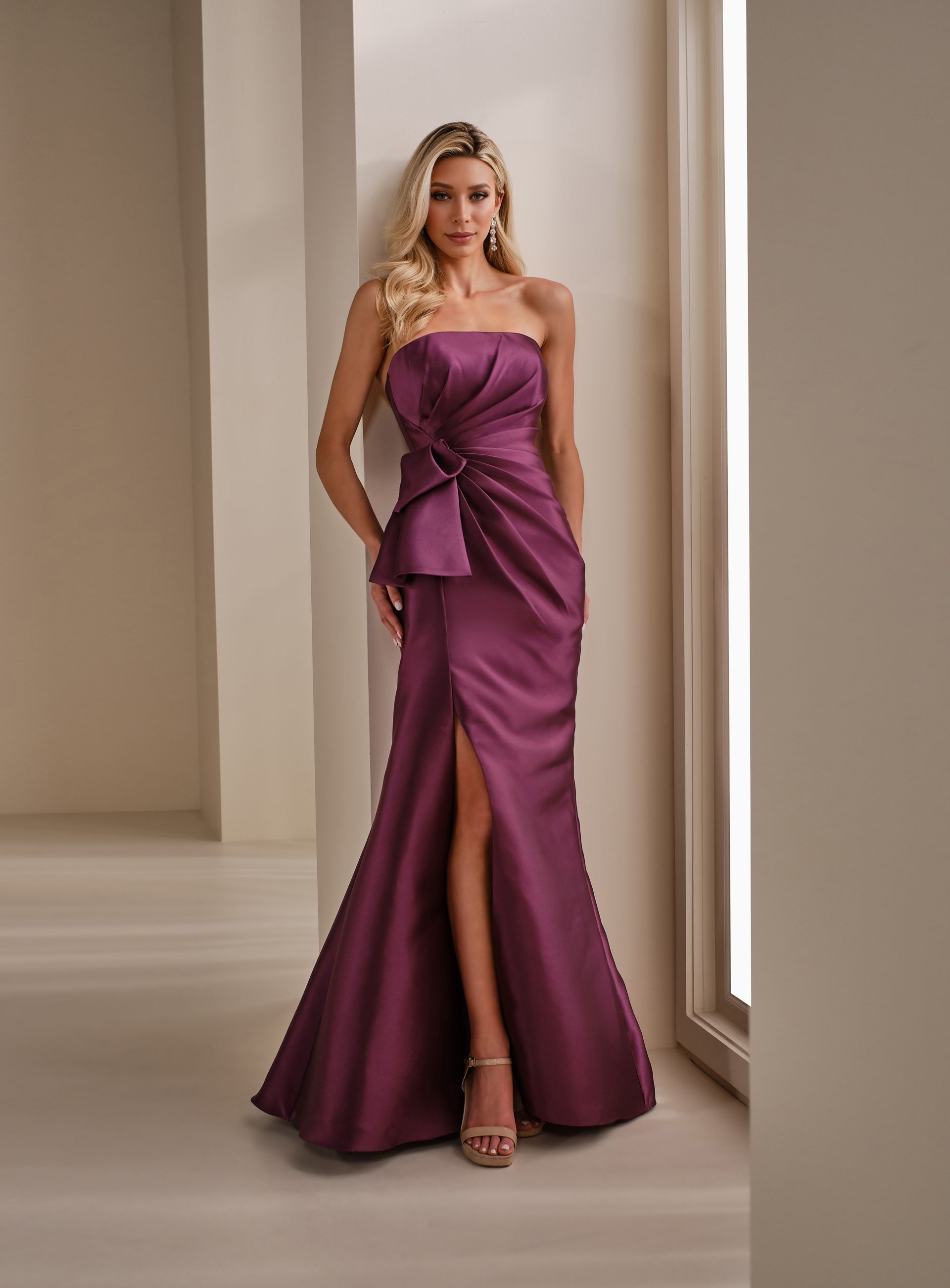 Woman in an olive green strapless gown standing in a bright studio with cream curtains.