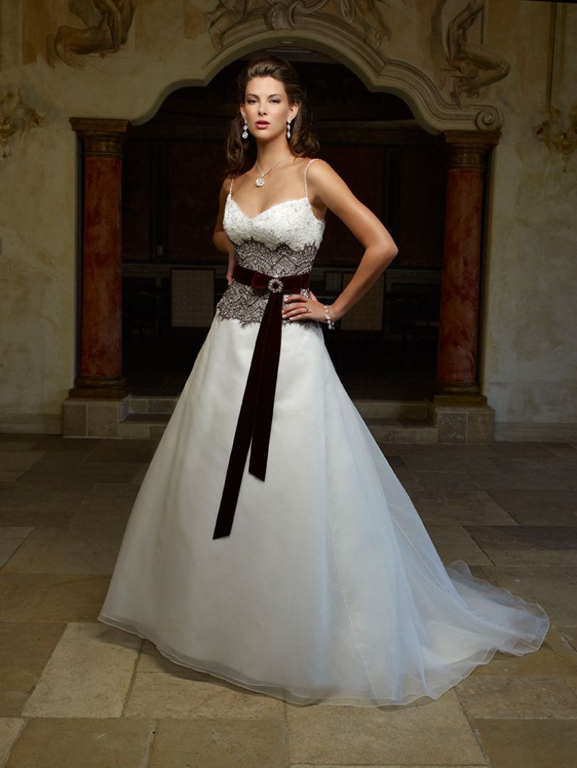 Woman in a white wedding gown with a brown waist sash, standing in a stone hallway with archways.