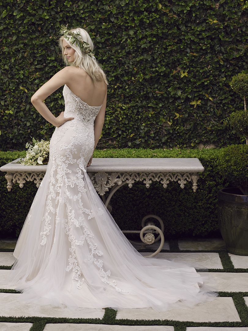 Woman in white strapless wedding dress, floral crown, posing in garden, standing by a decorative table.