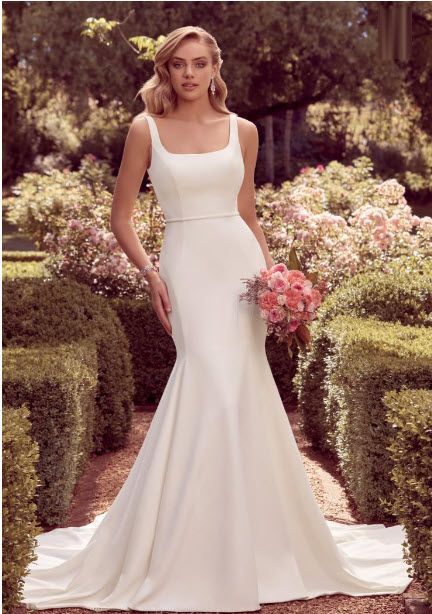 Woman in white wedding dress holding flowers, standing in garden.