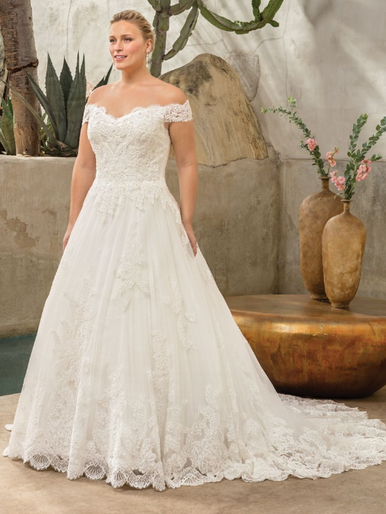 Woman wearing off-the-shoulder white lace wedding dress, standing outdoors.