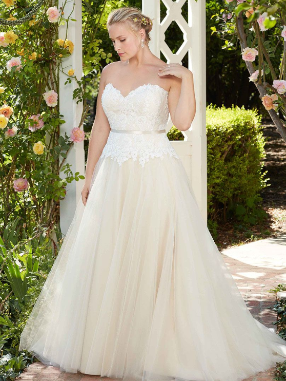Woman in a strapless ivory wedding gown stands near a white trellis.