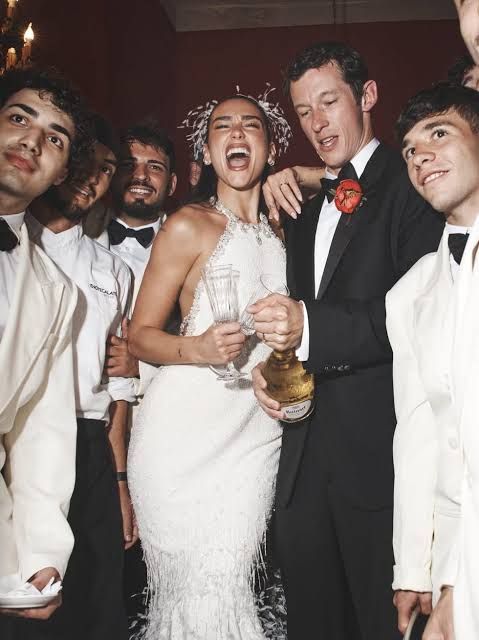 Wedding guests celebrating with champagne; the bride laughs in a white gown beside a groom in a black tuxedo. Wedding guests celebrating with champagne; the bride laughs in a white gown beside a groom in a black tuxedo.