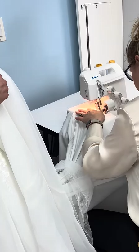 Person sewing white fabric on a sewing machine in a bright room Person sewing white fabric on a sewing machine in a bright room