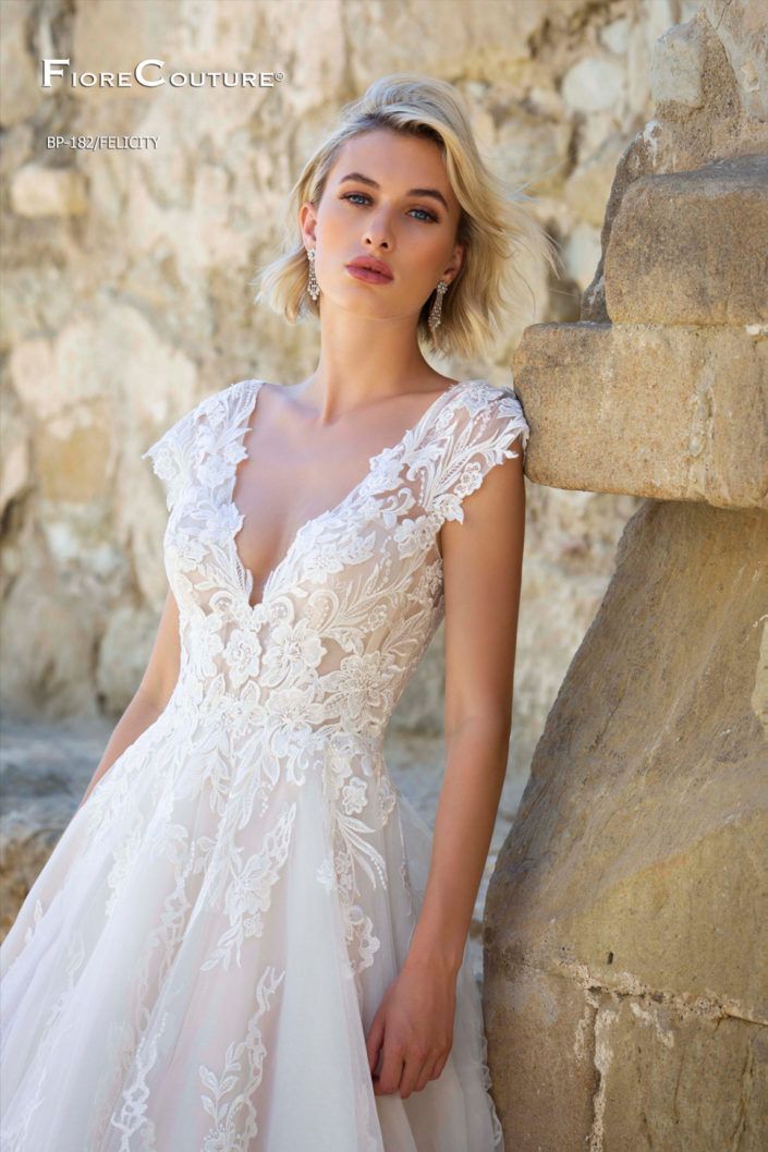 Woman in a white lace wedding dress leaning against a stone wall.