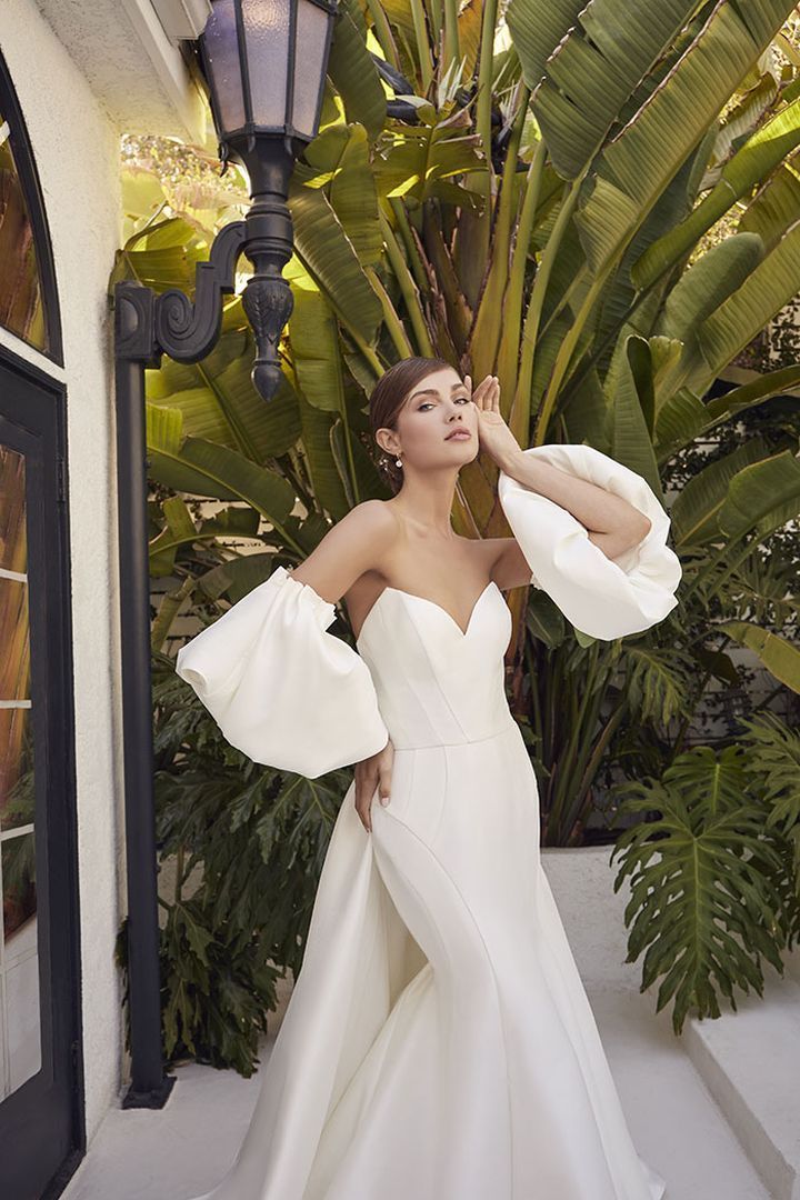 Woman in white strapless wedding gown with detachable sleeves, posing outdoors.