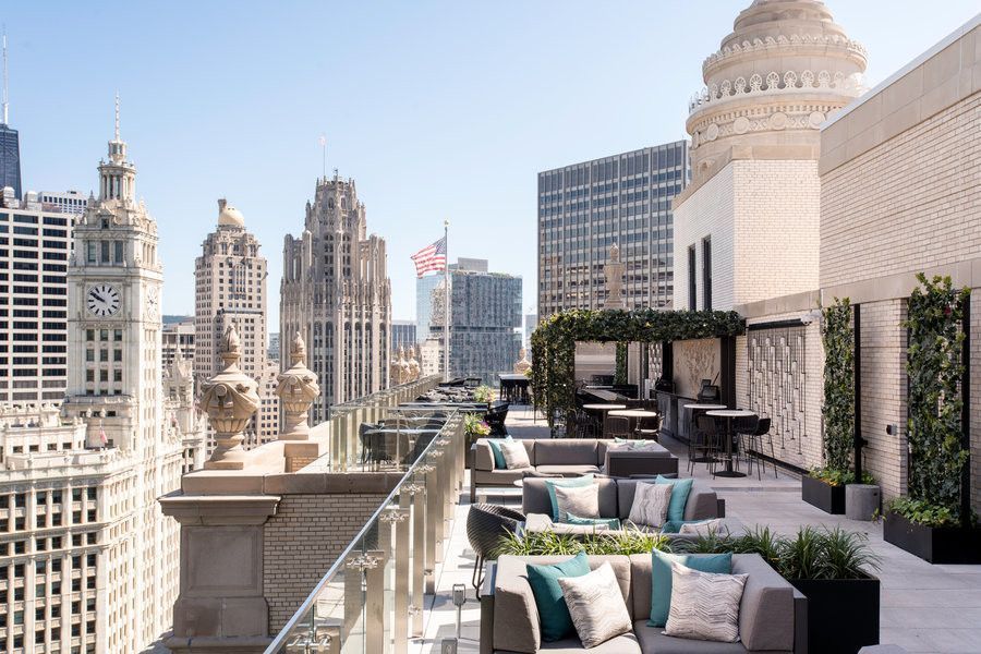 Rooftop lounge with city skyline views. Gray couches, turquoise pillows, and greenery on the terrace.