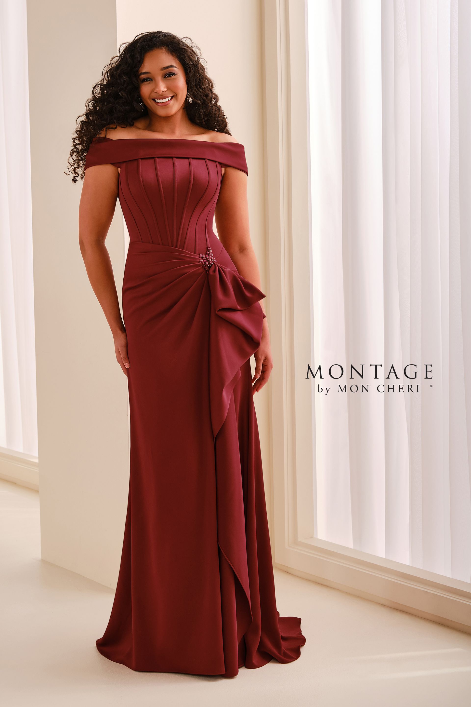 Woman in an off-shoulder olive green dress posing indoors against a light wall.