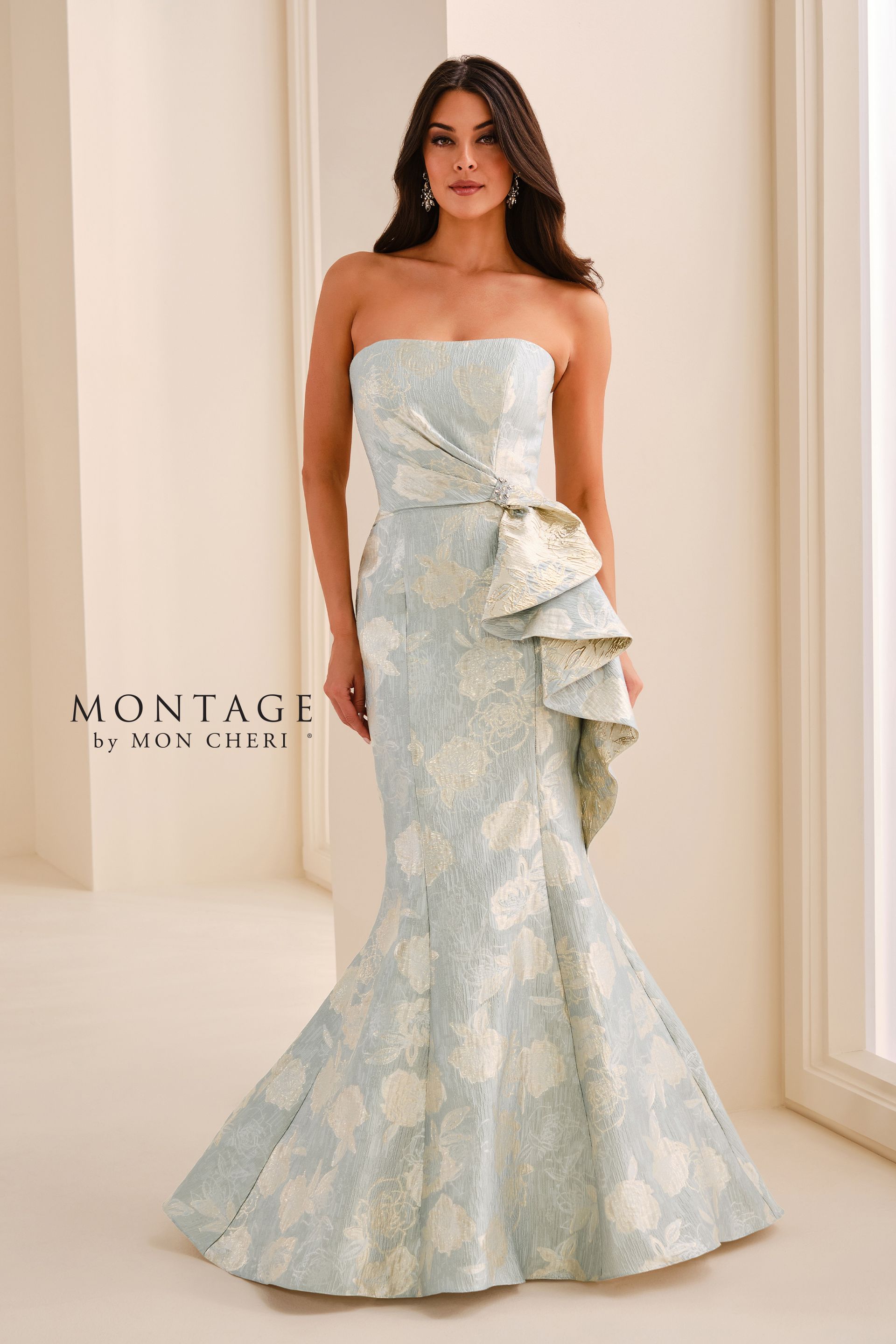 Woman in a strapless pale blue floral gown standing in a bright indoor setting with a ruffled side detail