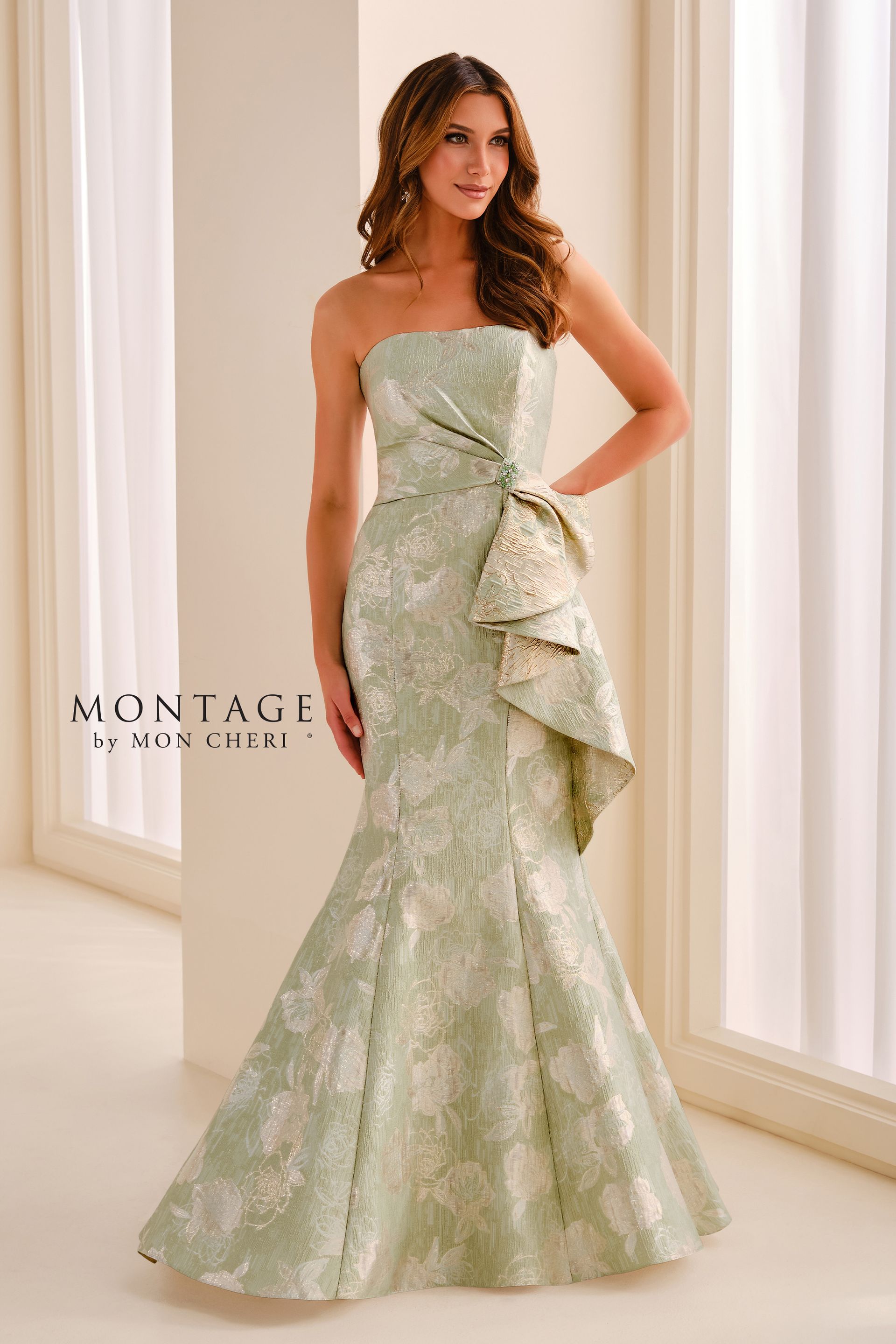 Woman in a strapless pale blue floral gown standing in a bright indoor setting with a ruffled side detail