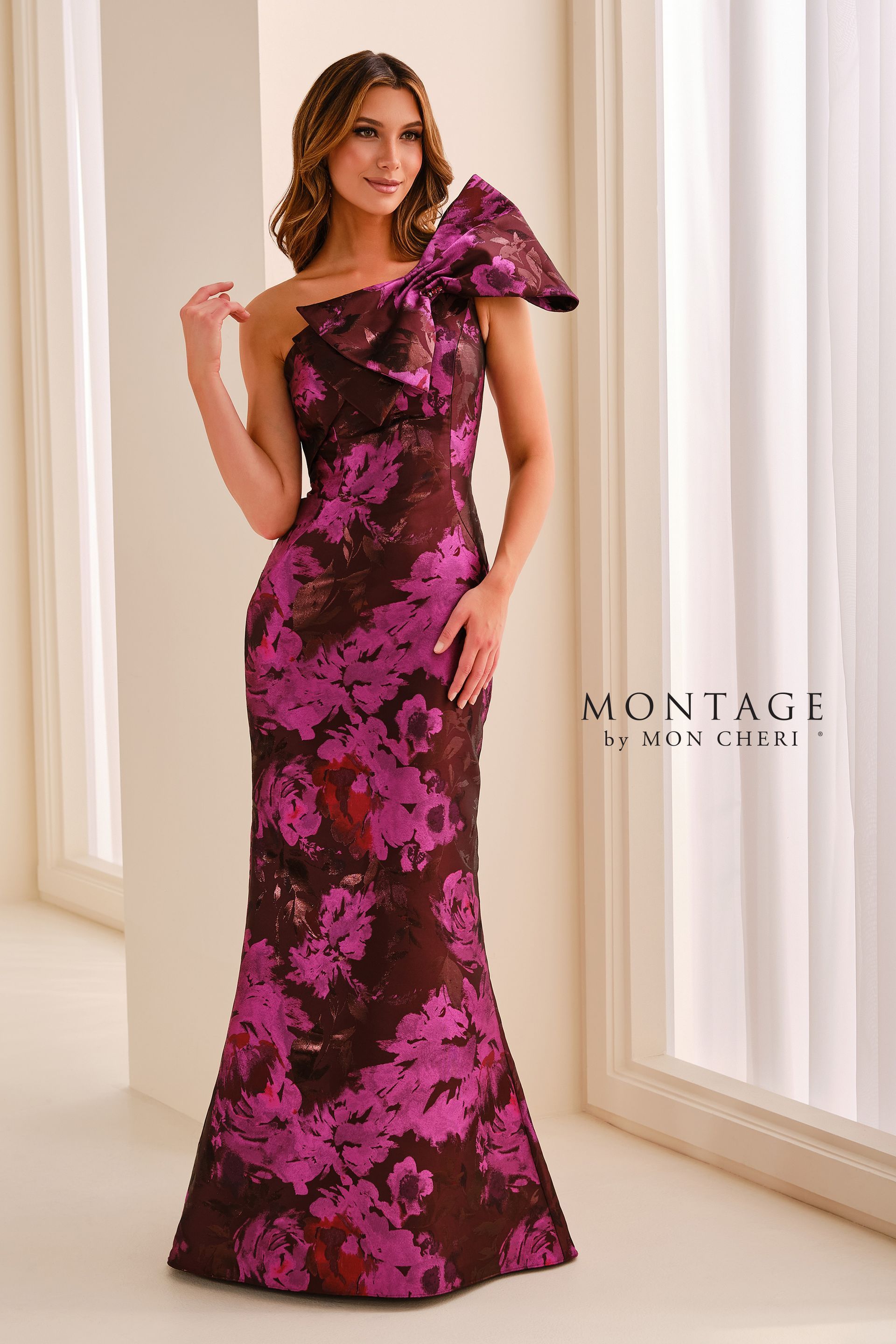 Woman in a blue-and-black floral gown standing in a bright room by a window.
