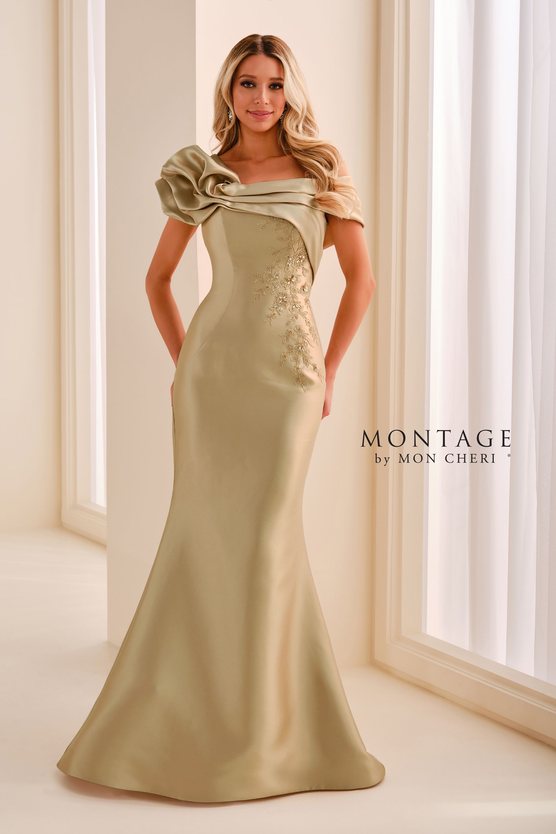 Woman in a teal off-shoulder gown standing in a bright room by a window.