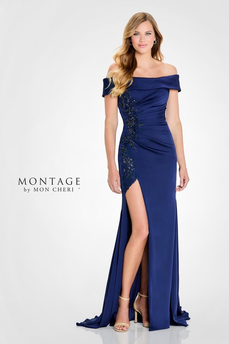 Woman in a navy off-the-shoulder gown with a high slit, standing against a white backdrop.