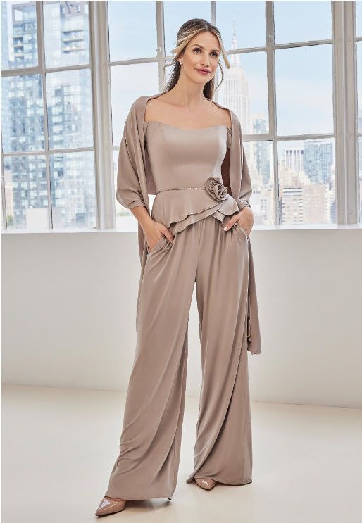 Woman in a beige pantsuit and shawl posing in front of a window.