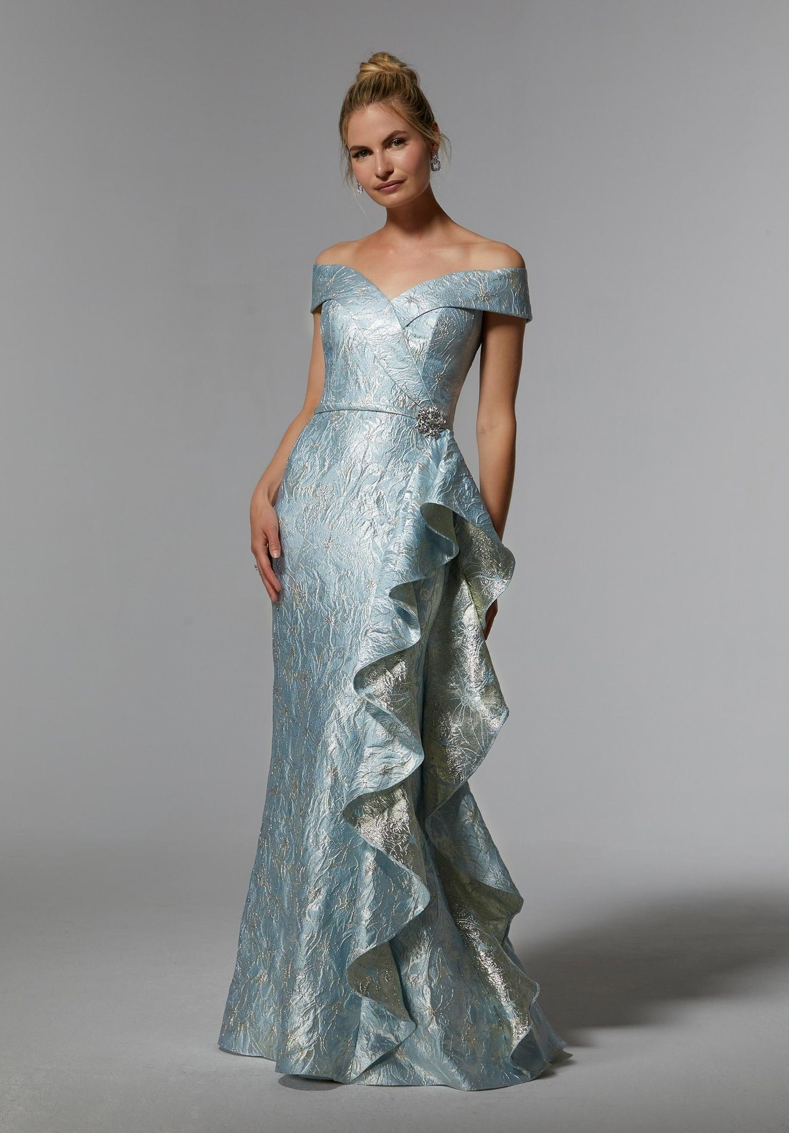 Woman in a light blue off-the-shoulder gown with ruffled side detail poses in a studio.