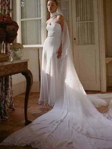 Woman in a white gown with a long train standing in a softly lit room near a window. Woman in a white gown with a long train standing in a softly lit room near a window.