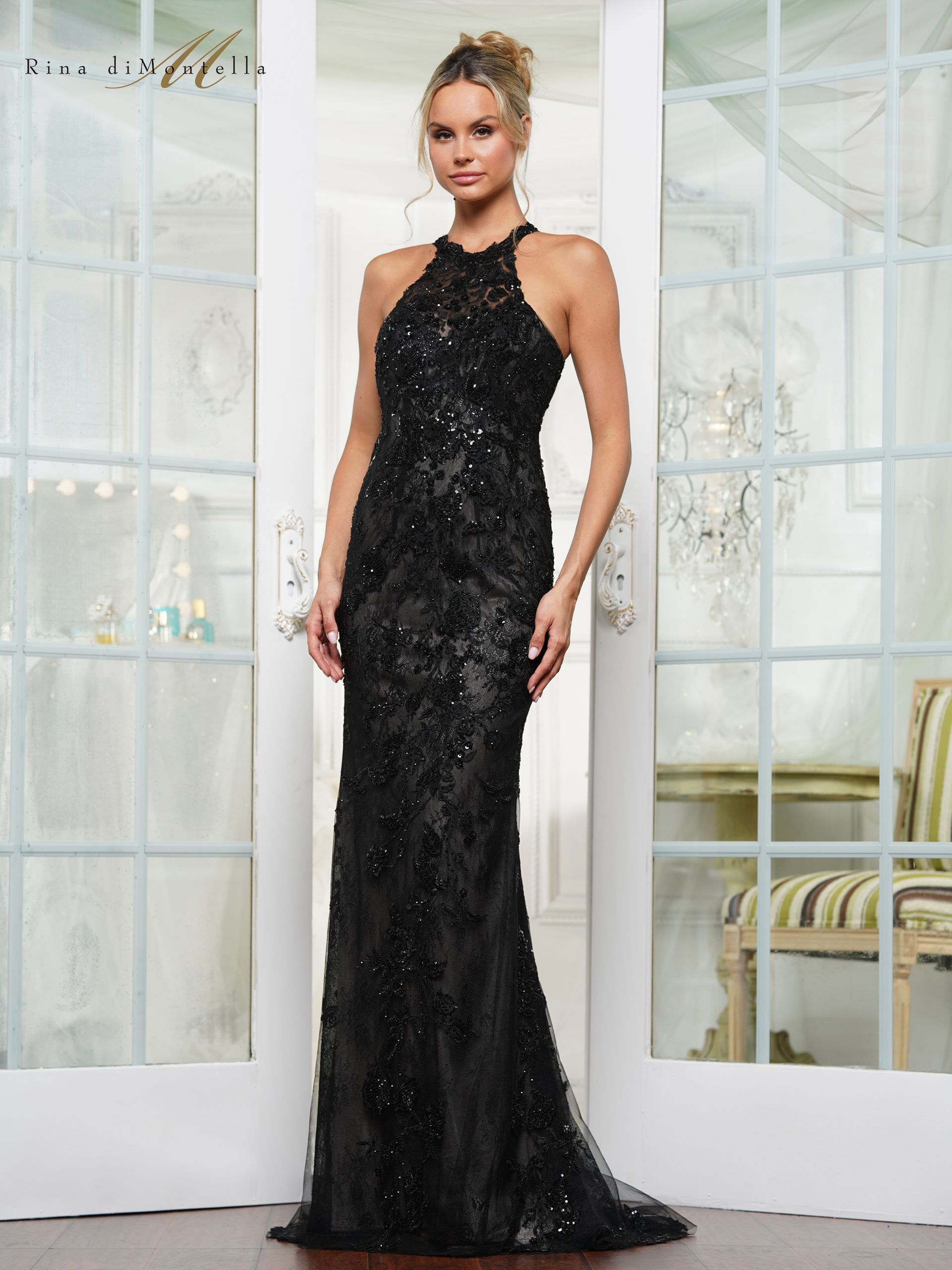 Woman in a black, beaded, halter-neck gown stands in front of a window.