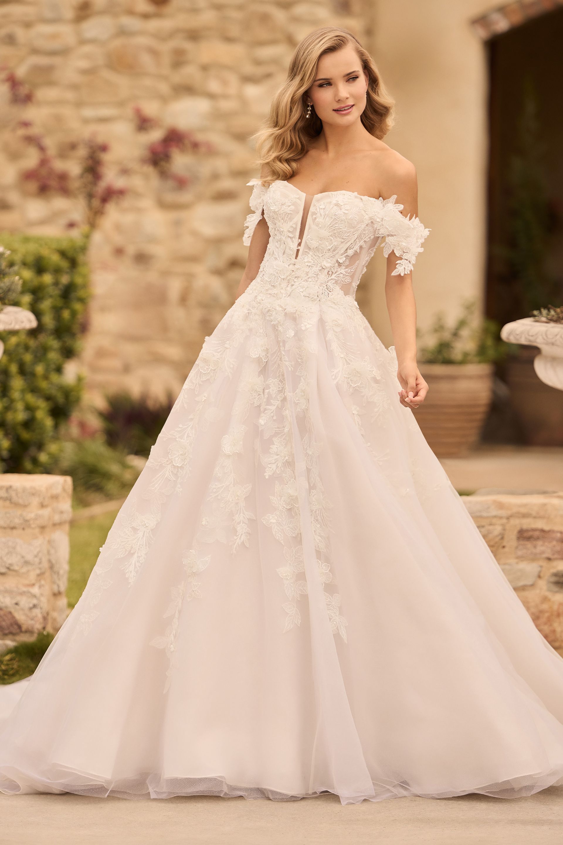 Woman in a white off-the-shoulder wedding dress posing outside.