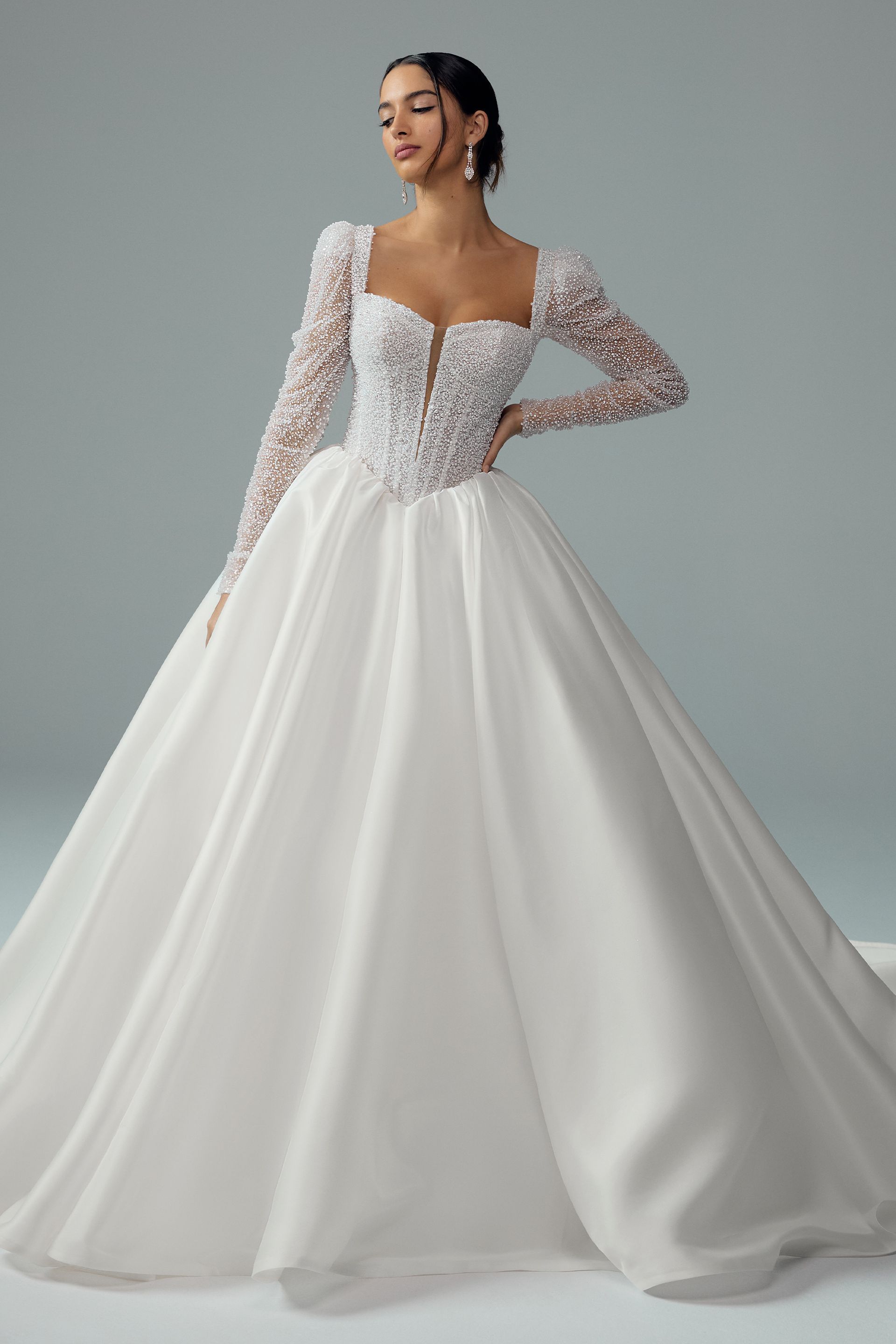 Woman in a white wedding gown with long, floral-sleeved bodice and a flowing skirt, posing.