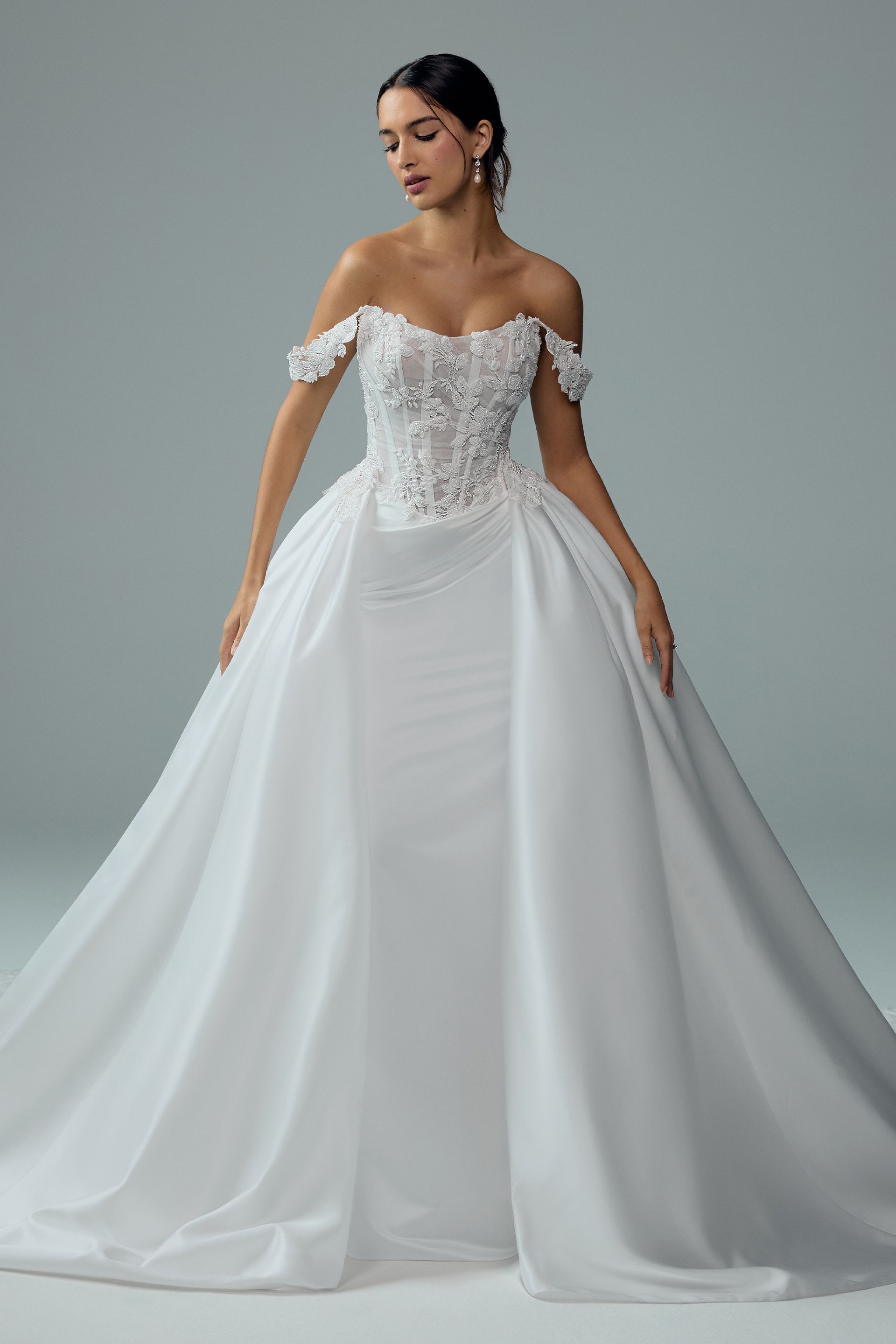 Woman in strapless white wedding dress with detachable skirt, standing on a pier, blue sky background.