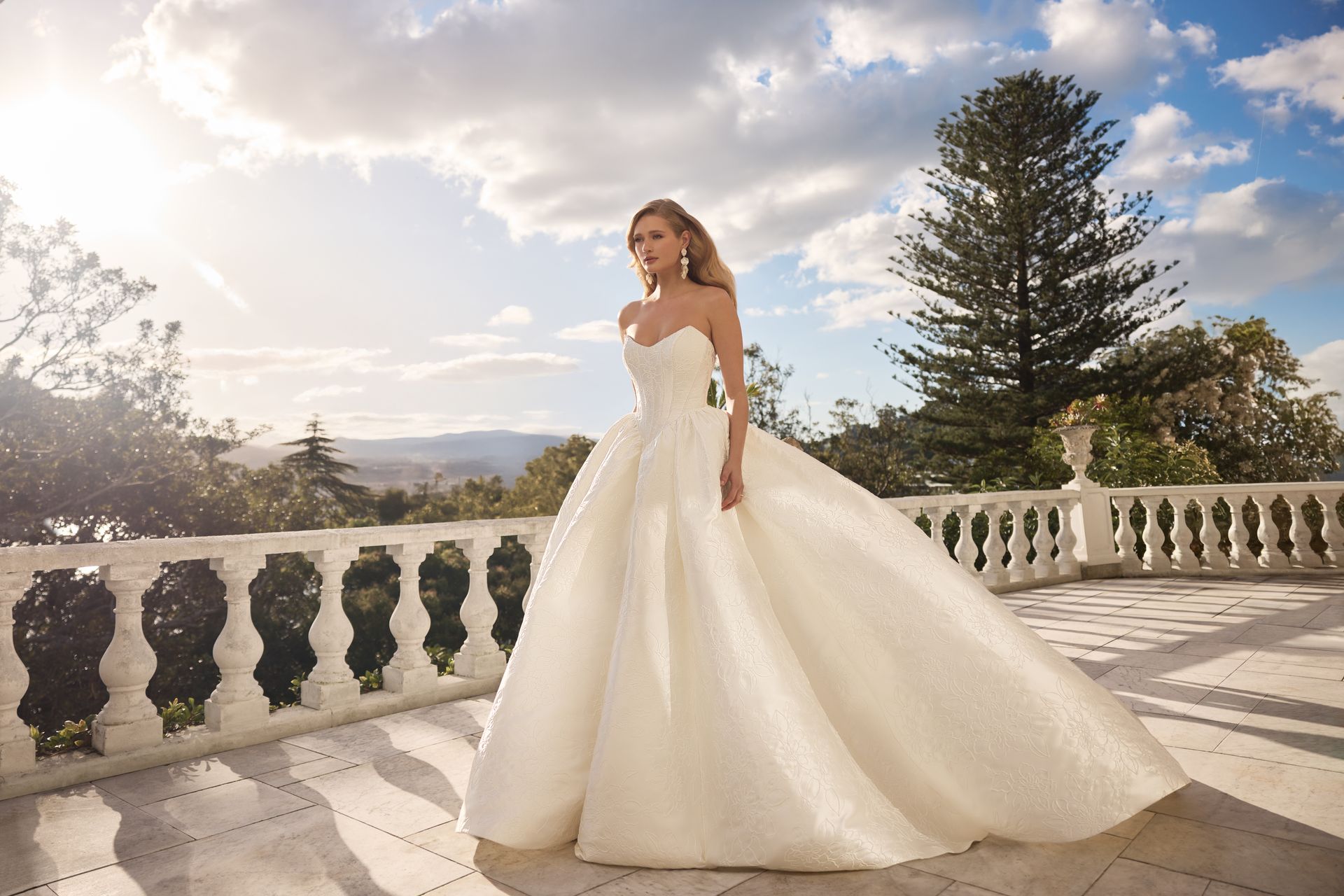Bride in a white wedding gown standing on a sunlit terrace with a scenic mountain view Bride in a white wedding gown standing on a sunlit terrace with a scenic mountain view