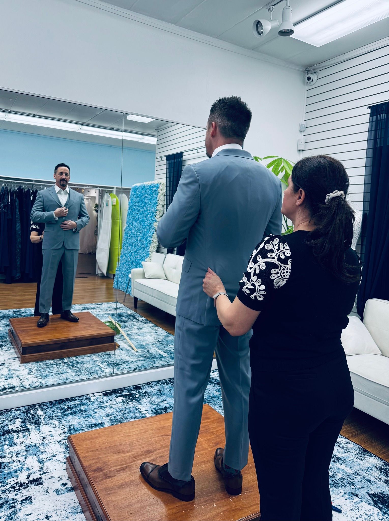 Man in a suit being fitted by a woman in a tailor shop. He stands on a platform in front of a mirror. Man in a suit being fitted by a woman in a tailor shop. He stands on a platform in front of a mirror.