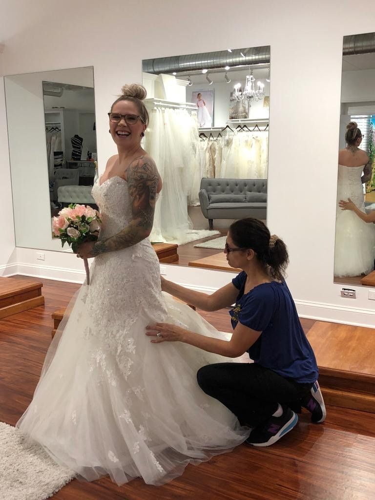 Woman in wedding dress being fitted by another woman in a bridal shop.