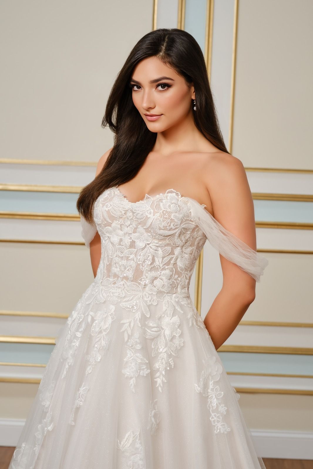 Woman in a strapless white lace gown posing against a gold-accented wall