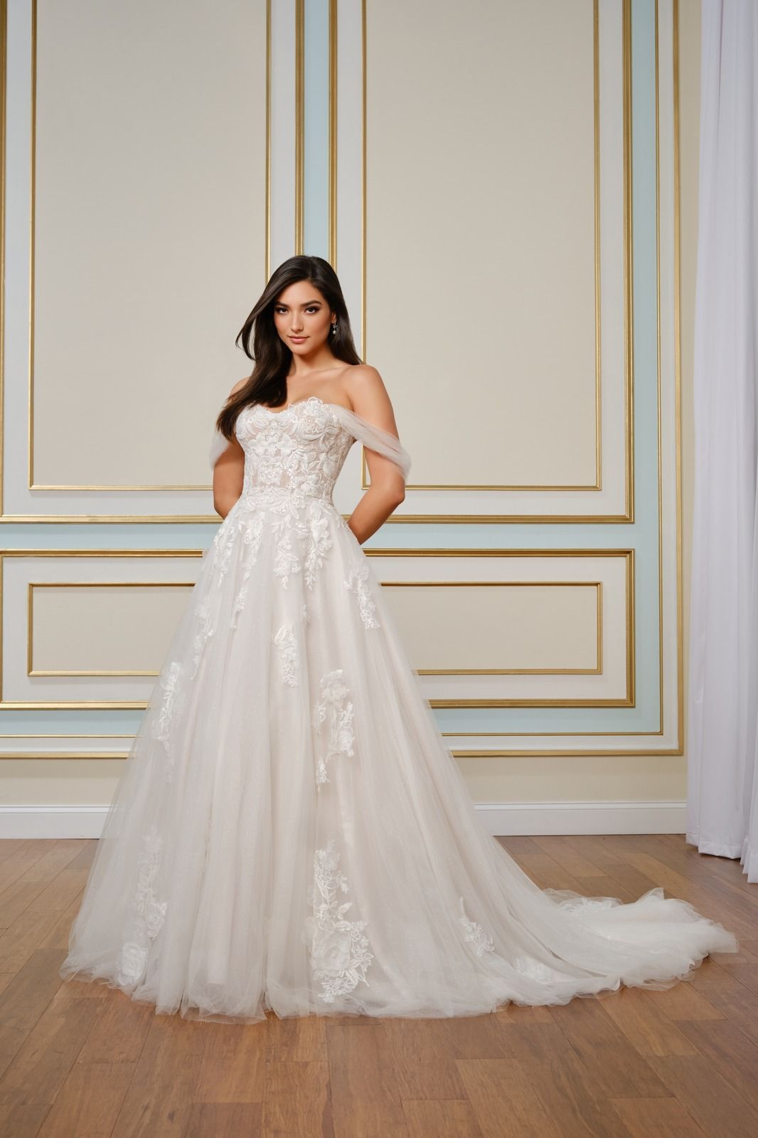 Woman in a strapless white lace gown posing against a gold-accented wall