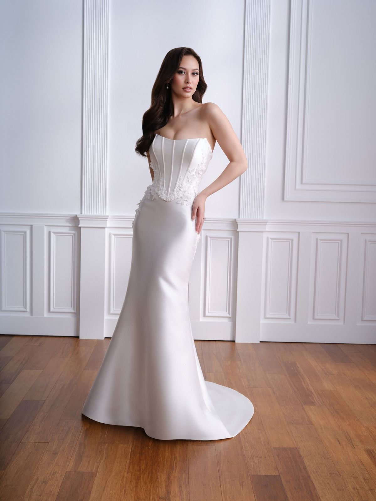Woman in a white strapless gown standing in a bright room with paneled walls and wood floors
