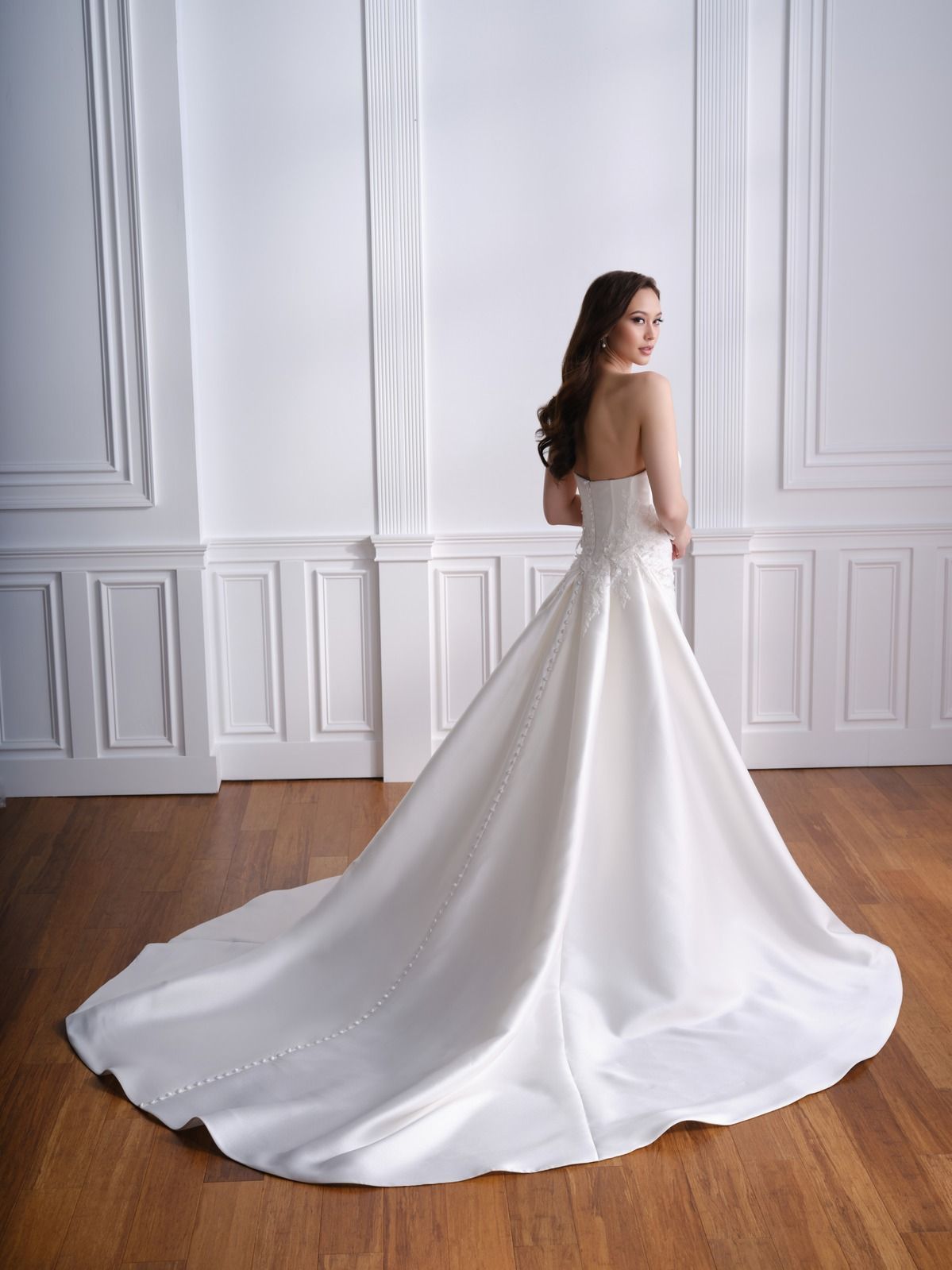 Woman in a white gown standing in a bright room with a long flowing train