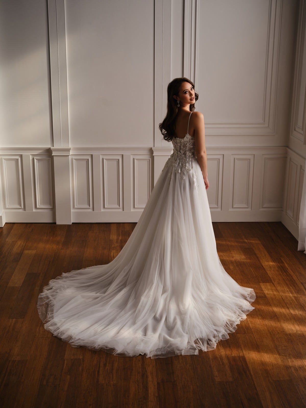 Woman in a white lace wedding gown standing in a bright room with wood floors and paneled walls