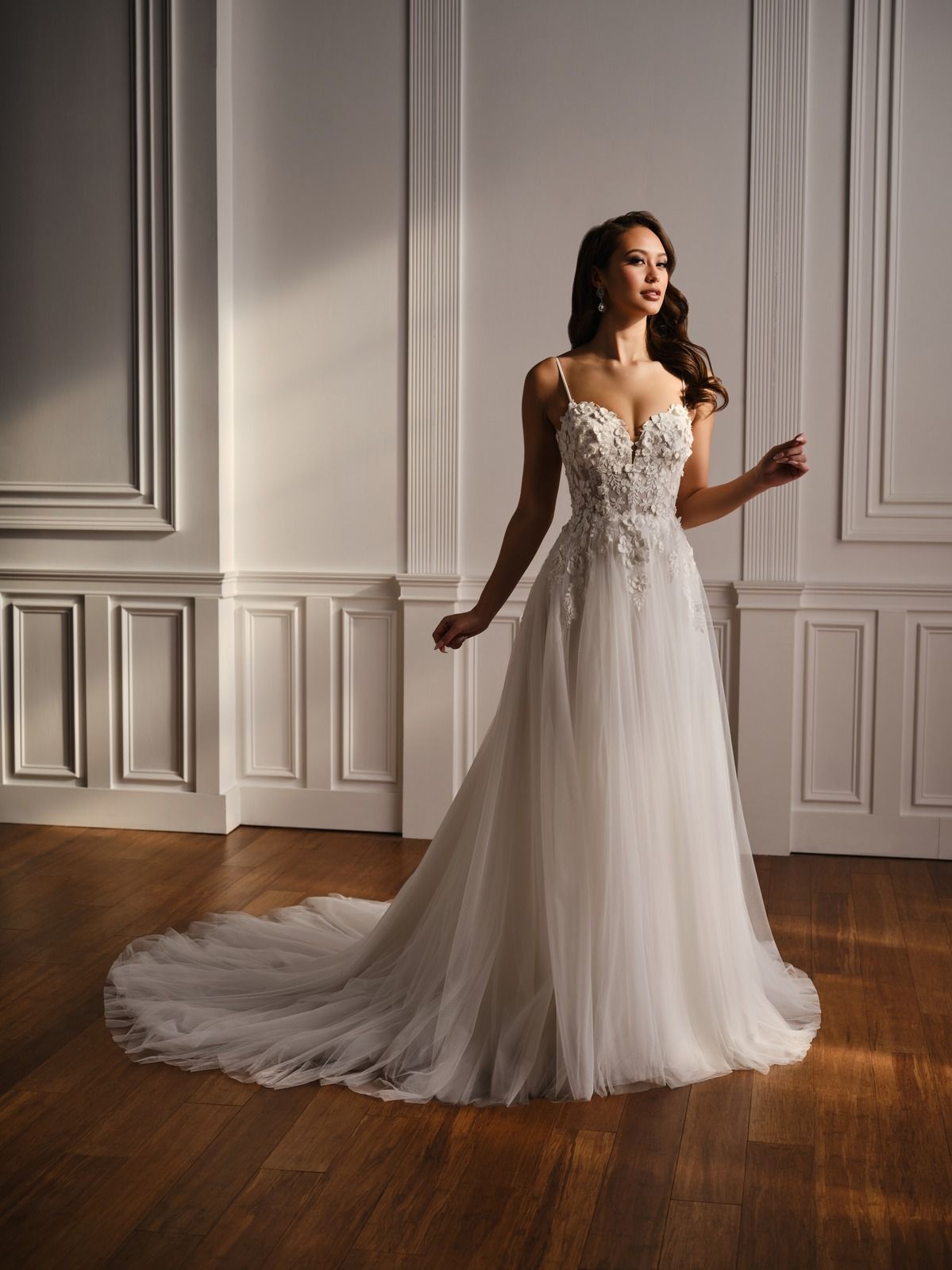 Woman in a white lace wedding gown standing in a bright room with wood floors and paneled walls