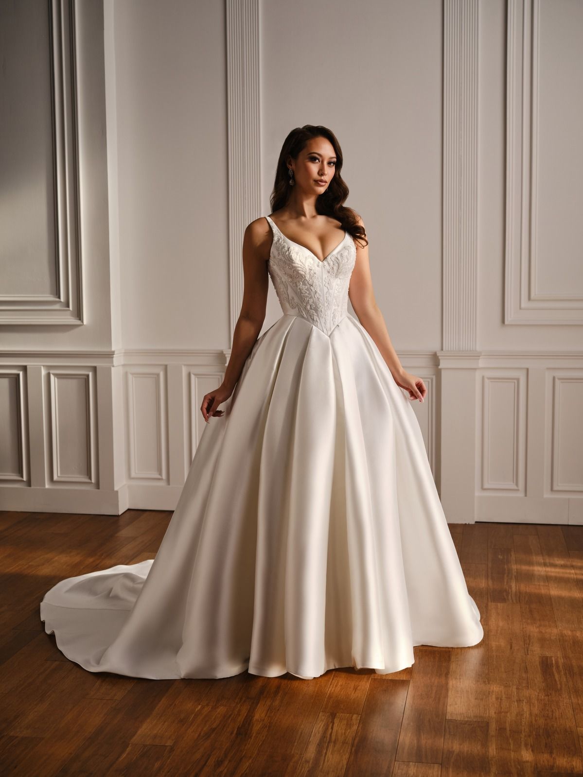 Woman in a white lace ball gown posing indoors against a paneled wall.