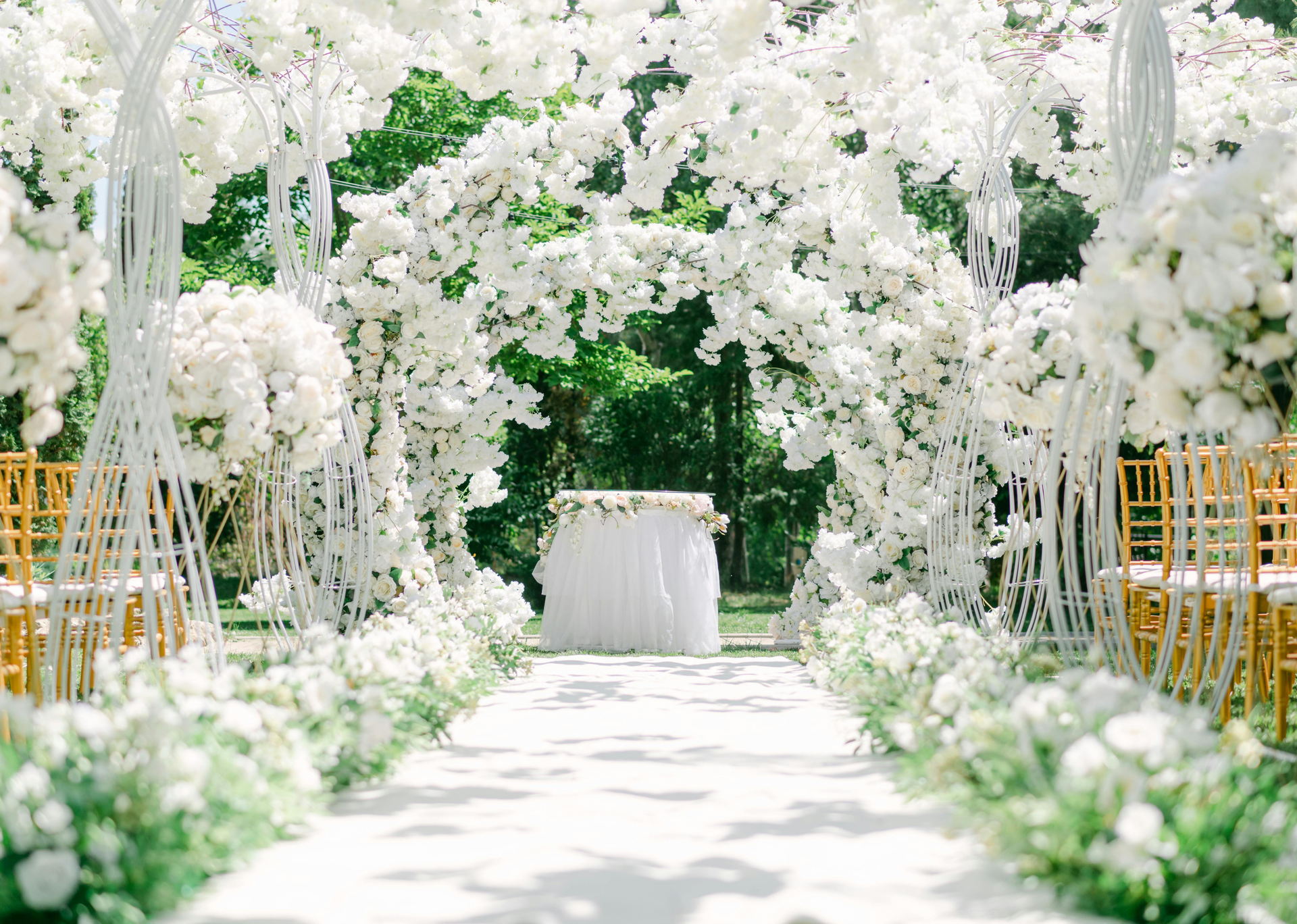 White floral wedding aisle with arching flower arrangements and a white table at the end