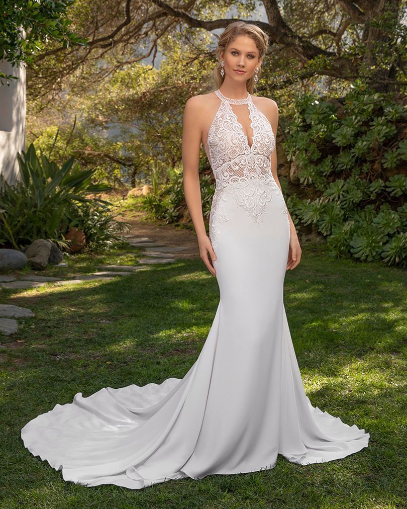 Woman in a white beaded halter gown standing in a garden, with a long flowing train. Woman in a white beaded halter gown standing in a garden, with a long flowing train.