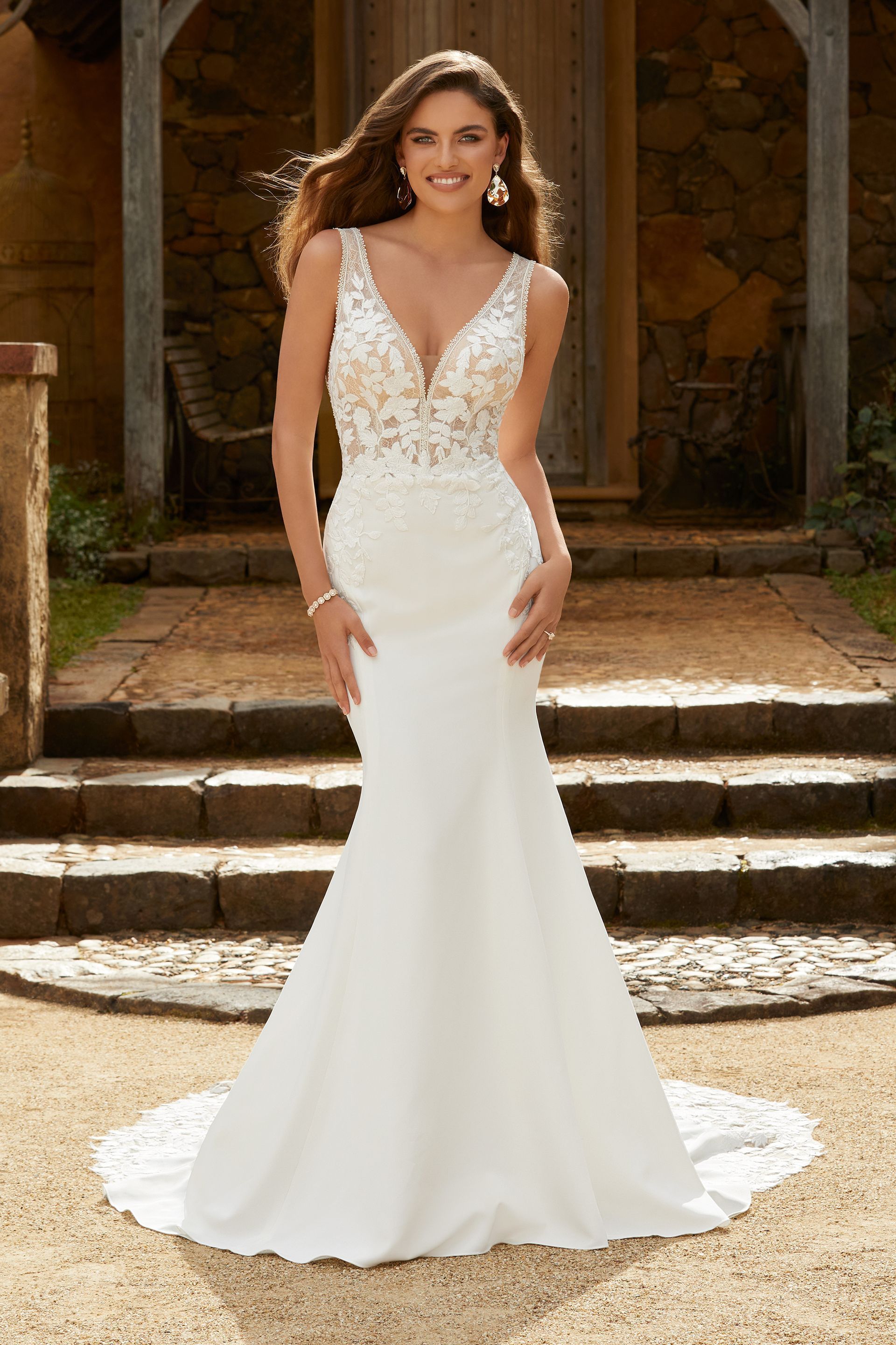 Woman in white wedding dress with beaded bodice, standing outdoors, smiling.
