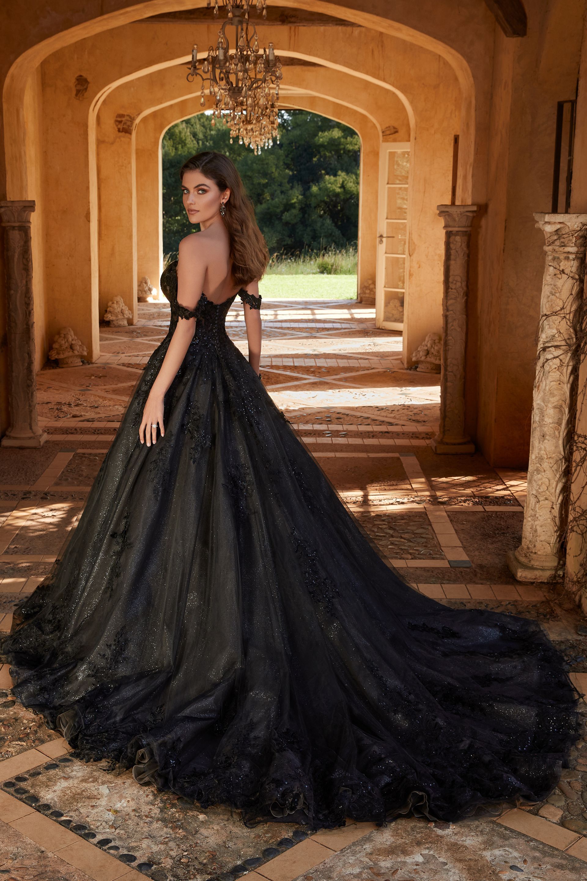 Woman in a black off-shoulder gown with a long train, standing in a stone archway.