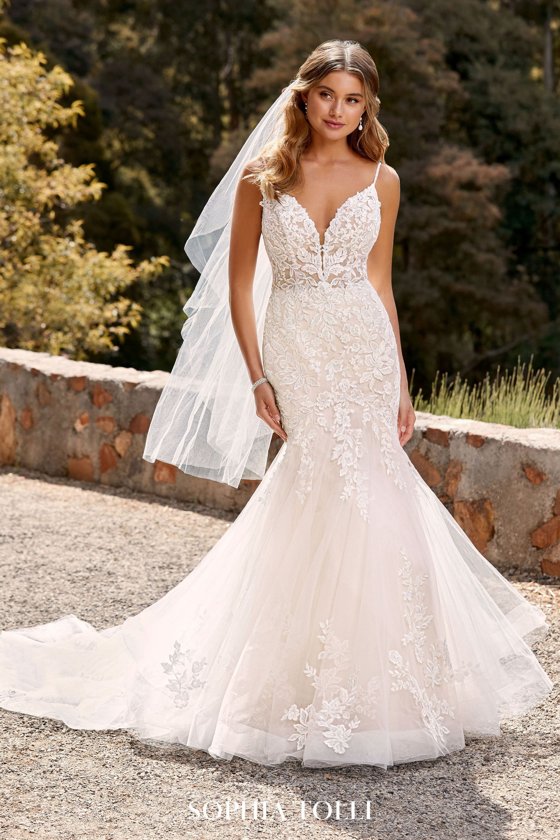 Woman in a white lace mermaid wedding dress, veil, and jewelry outdoors.