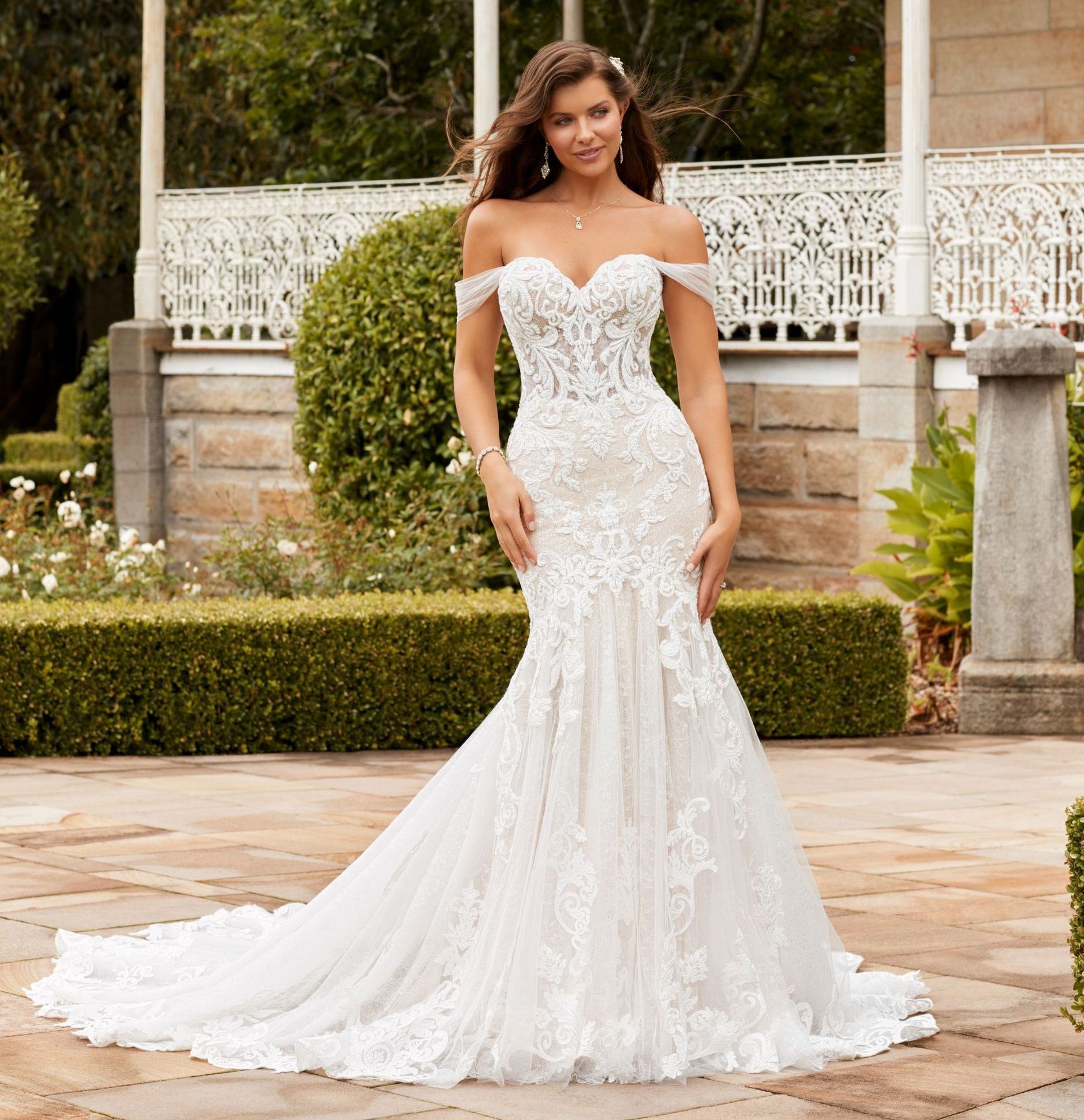 Woman in an off-the-shoulder white wedding dress, posing in a garden setting.